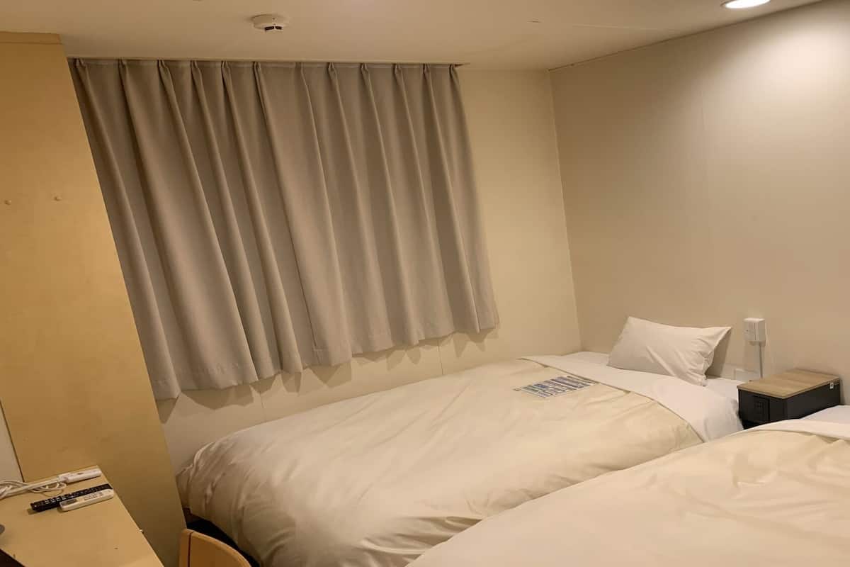 Ein Hotelzimmer mit zwei Betten, einem Nachttisch, einer Lampe und einem Fenster mit Vorhängen.