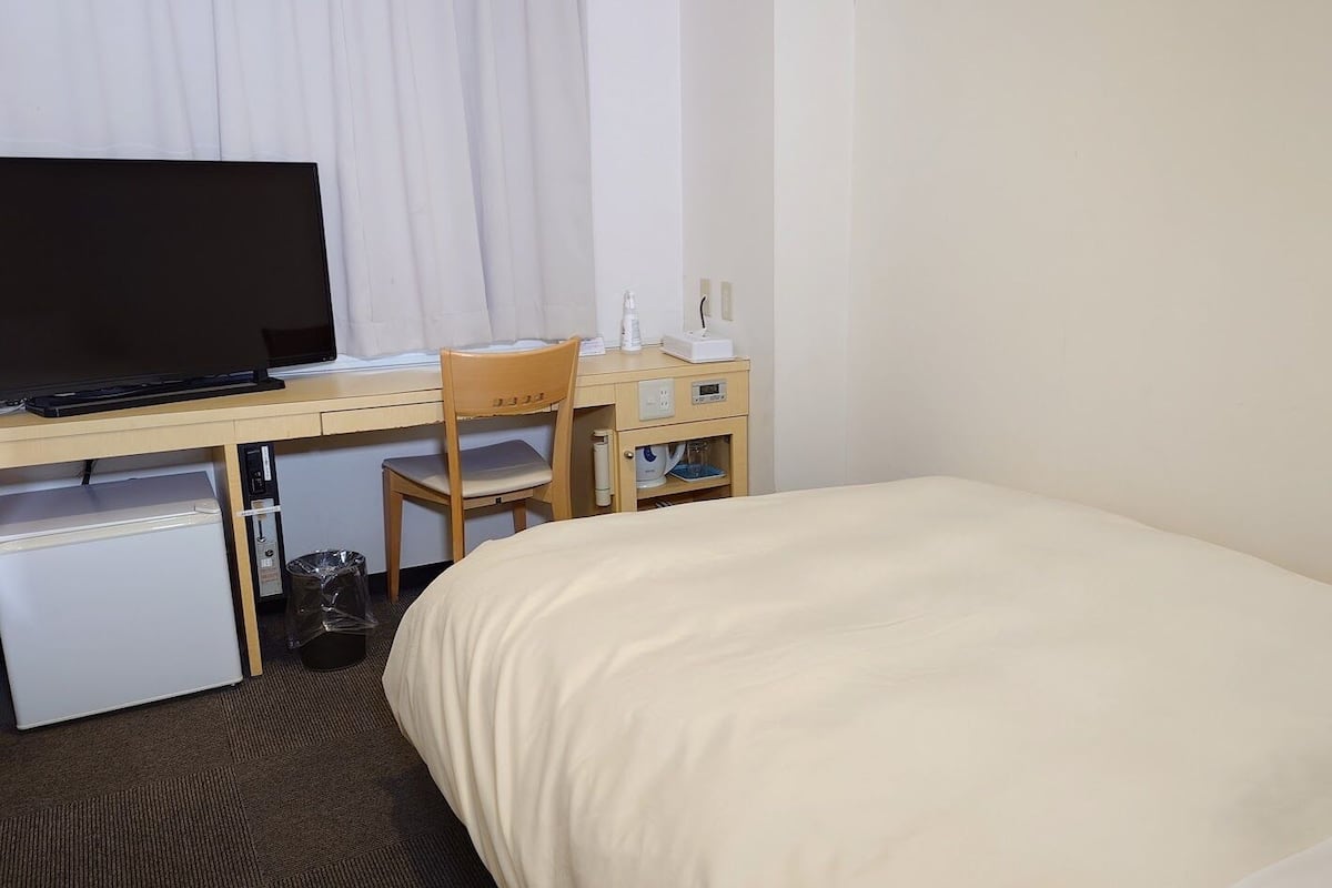 Ein Hotelzimmer mit Bett, Schreibtisch mit Computer, Stuhl, kleinem Kühlschrank und Fernseher.