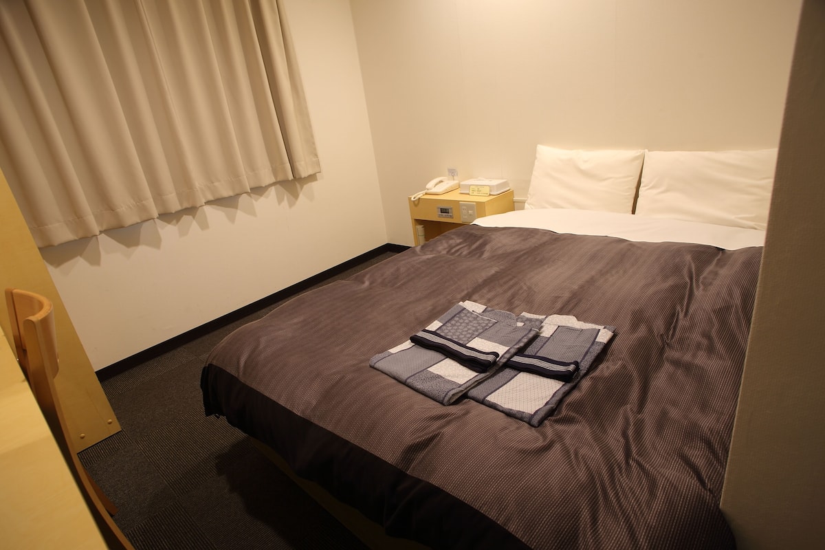 Ein Hotelzimmer mit einem Bett, einem Nachttisch mit Telefon und Lampe sowie einem Fenster mit Vorhängen.