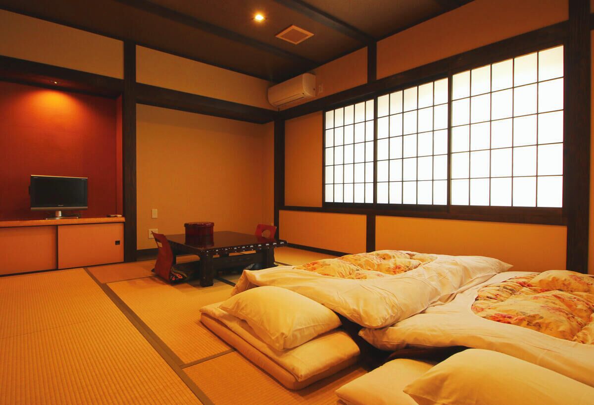 Perinteinen japanilainen huone, jossa on tatamimatto, futon-patja, matala pöytä ja liukuovi, jossa on ruudukkomainen kuvio.