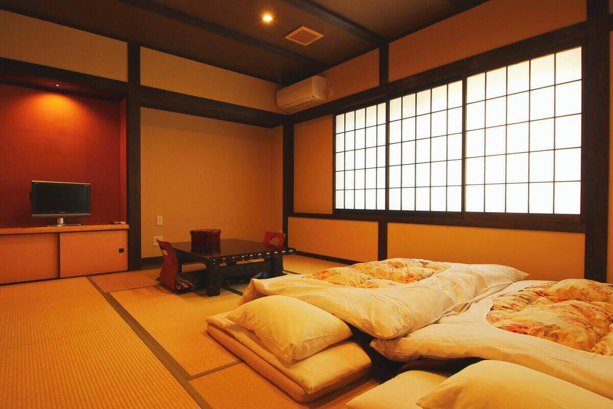 Une pièce de style japonais traditionnel, avec un sol recouvert de tatamis, un futon servant de lit, une petite table basse et une porte coulissante à motifs géométriques.