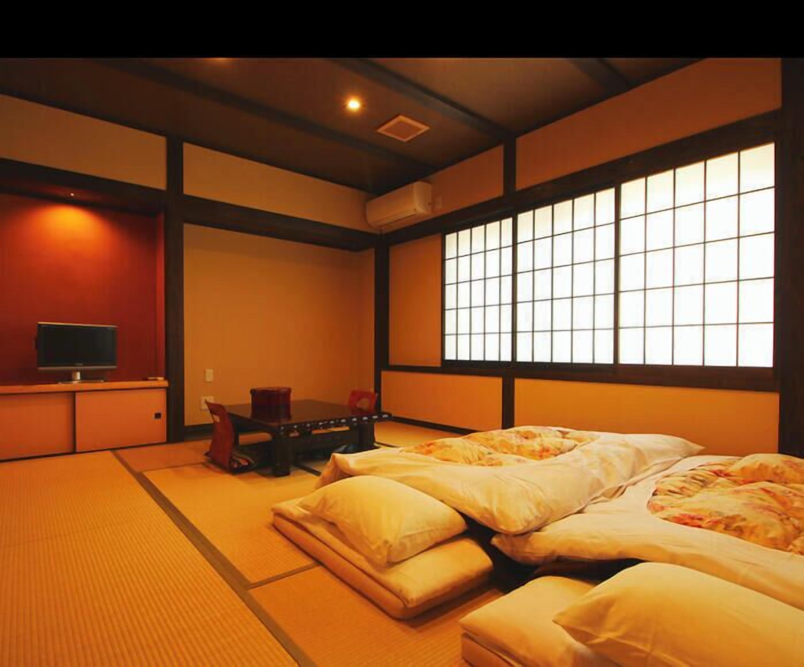 Ein traditioneller japanischer Raum mit Tatami-Bodenbelag, einem Futon und einer Rutschtür. Ein Fernseher ist ebenfalls vorhanden.