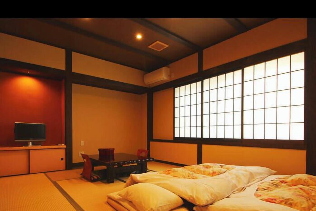 Une pièce de style japonais traditionnel, avec un sol recouvert de tatamis, un futon servant de lit, une télévision et une porte coulissante.