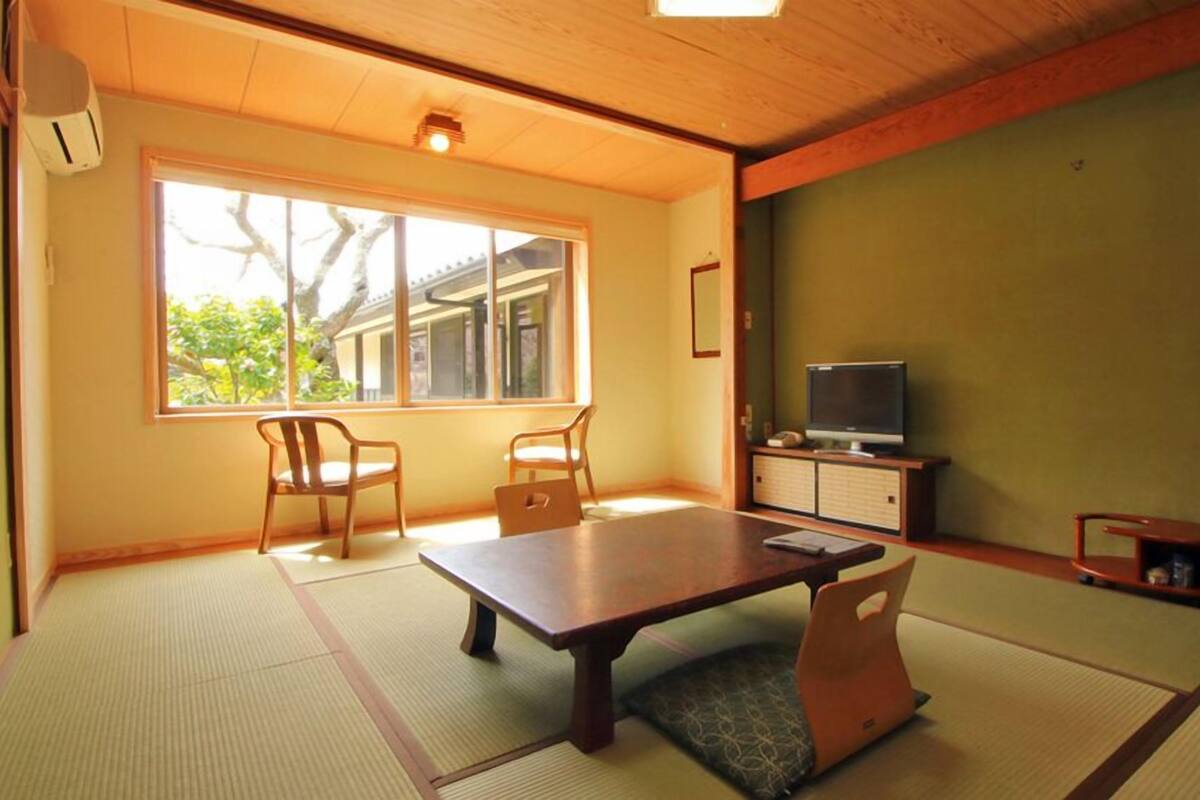 Une pièce de style japonais traditionnel, avec un sol recouvert de tatamis, une table basse, deux chaises, un téléviseur et un meuble.