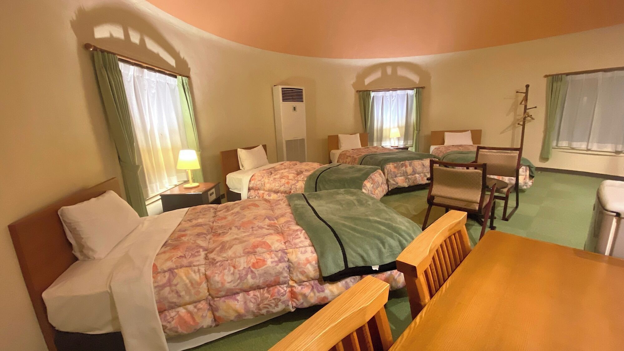 A hotel room with two beds, a desk, a chair, a lamp, and a window with curtains.
