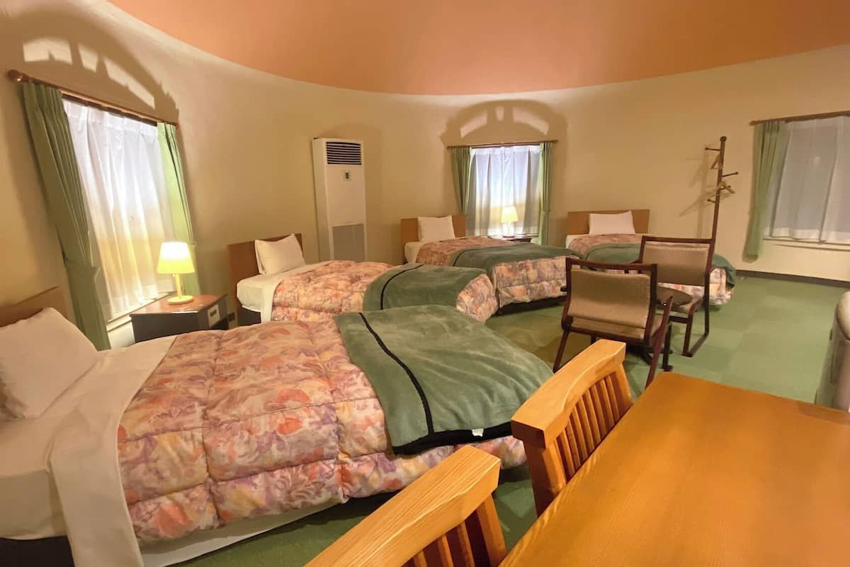 Ein Hotelzimmer mit zwei Betten, einem Schreibtisch, einem Stuhl, einer Lampe und einem Fenster mit Vorhängen.