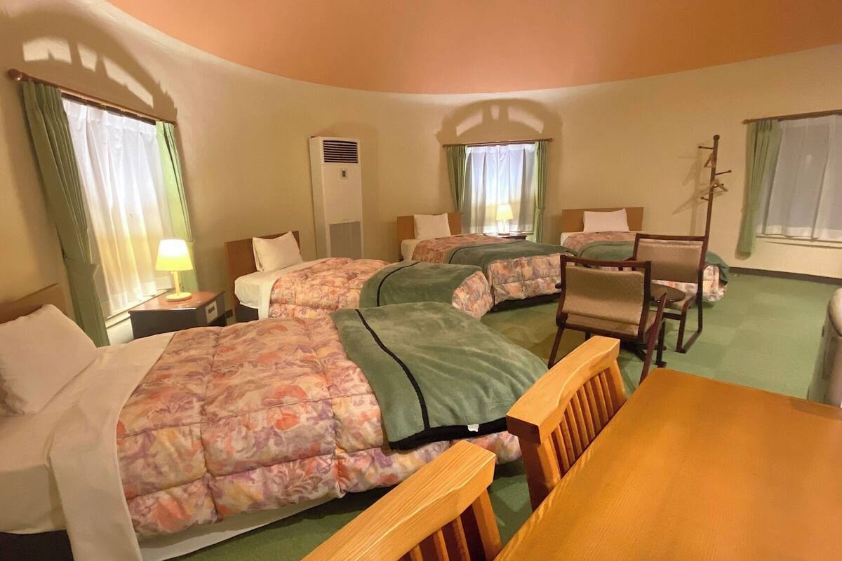 A hotel room with two beds, a desk, a chair, a lamp, and a window with curtains.