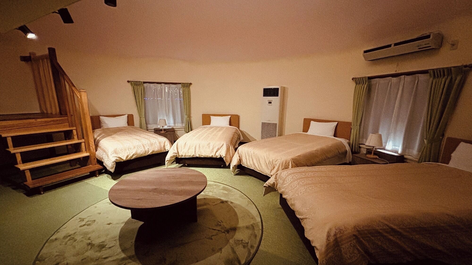 A hotel room with four beds, a wooden bench, a round table, and an air conditioning unit.
