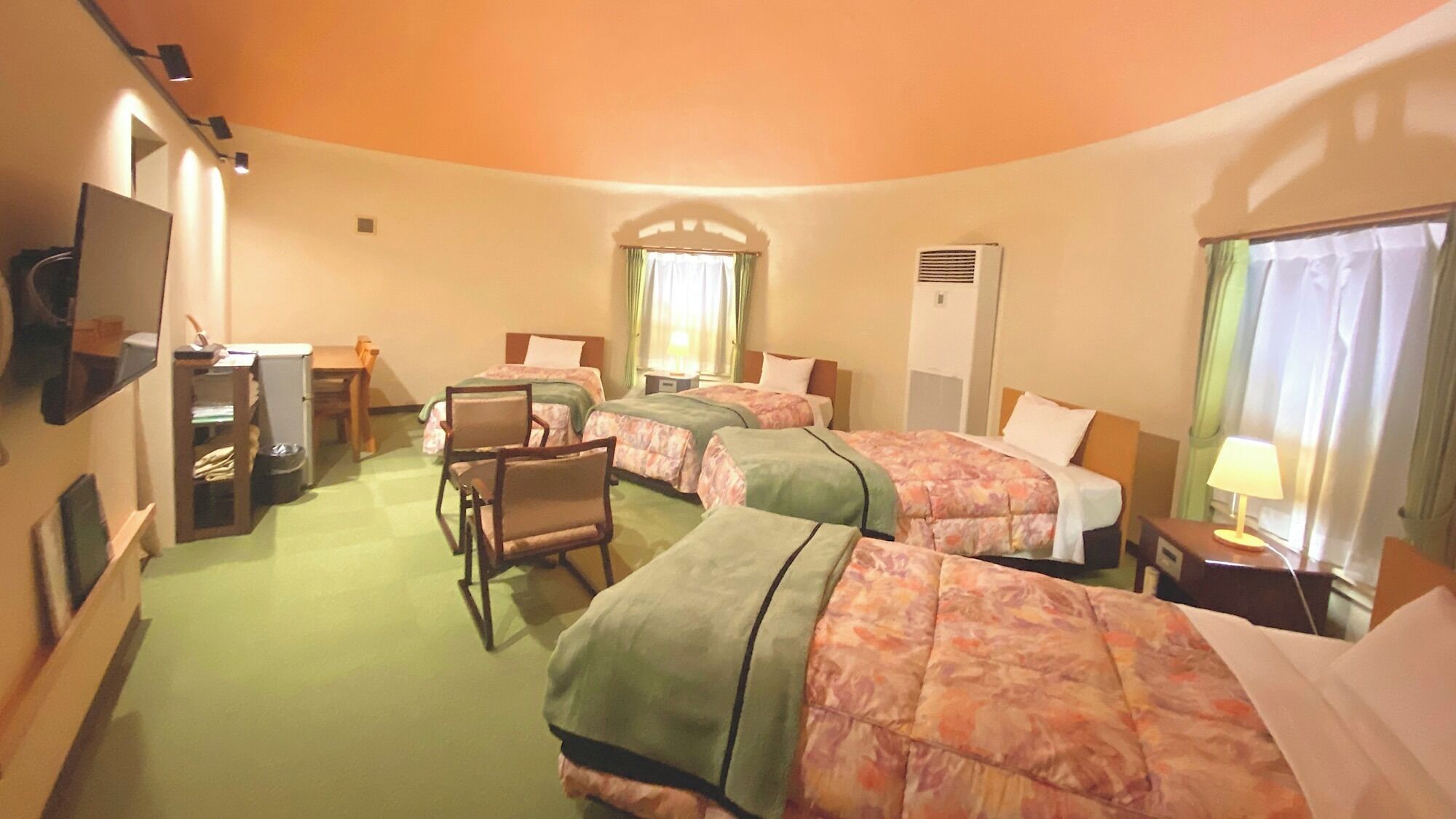 A hotel room with three beds, a desk, a chair, a television, and a window with curtains.