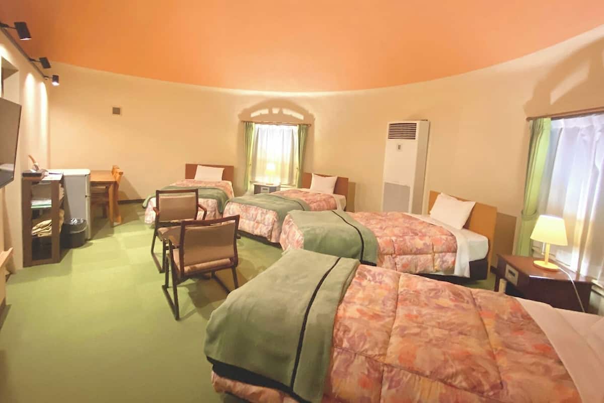 Ein Hotelzimmer mit drei Betten, einem Schreibtisch, einem Stuhl, einem Fernseher und einem Fenster mit Vorhängen.