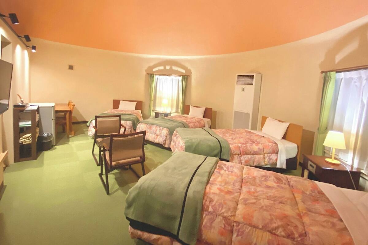 A hotel room with three beds, a desk, a chair, a television, and a window with curtains.