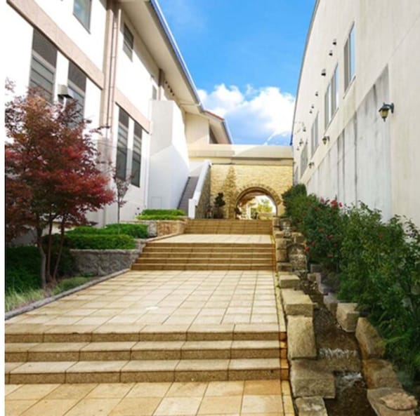A pathway leading to a building with a stone archway, surrounded by greenery and stone walls. - Shuzenji Tokinosumika Hotel Olive Tree/ Hyakuwarai (Izunokuni)