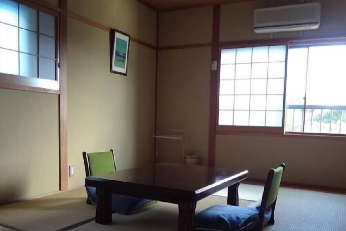 Una habitación con tatami, una mesa baja y sillas, un cuadro en la pared y una ventana con vistas.
