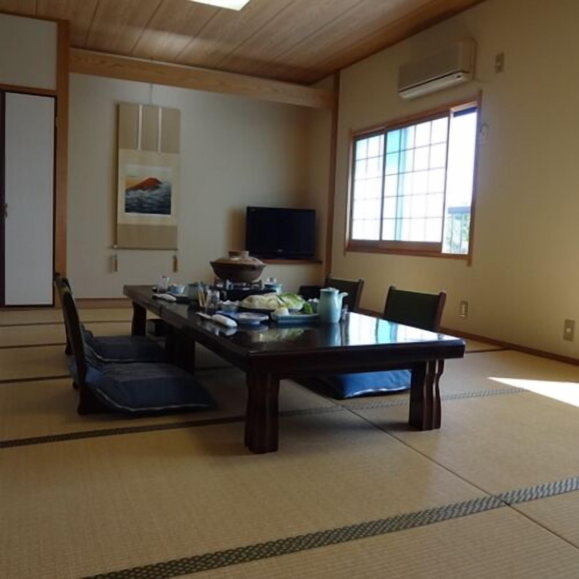A traditional Japanese room with tatami flooring, a low table with cushions, a television, and a window with a view.