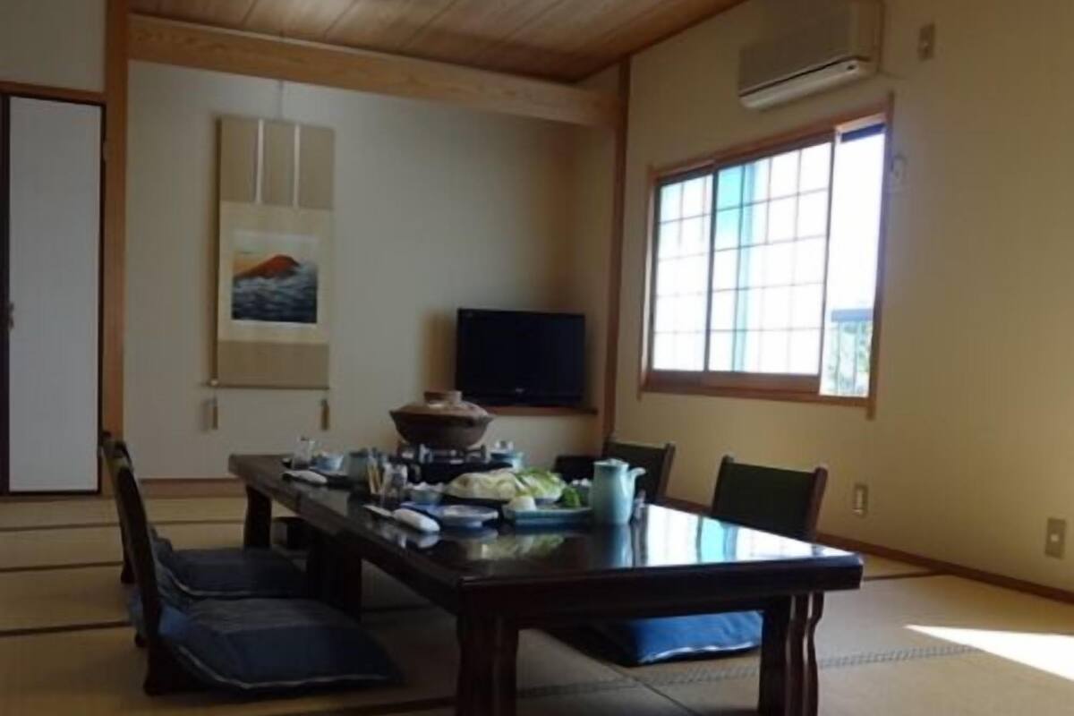 Una habitación japonesa tradicional con suelo de tatami, una mesa baja con cojines, un televisor y una ventana con vistas.