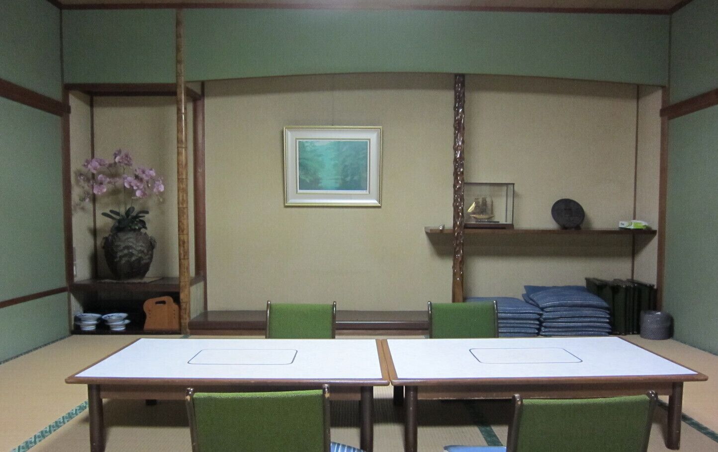 A traditional Japanese room with tatami flooring, a low table, and green chairs.