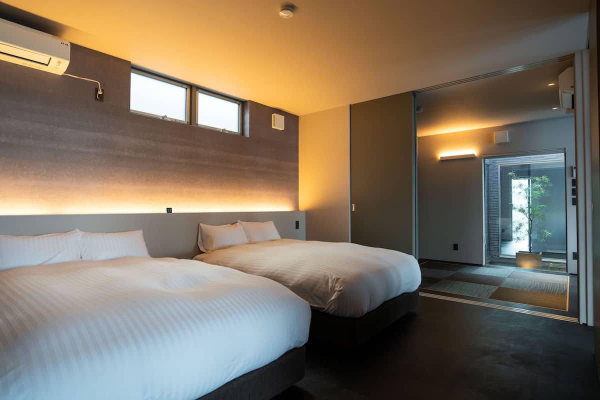 Une chambre d’hôtel moderne avec deux lits, une grande fenêtre et une porte coulissante donnant sur un balcon.