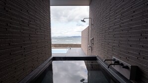 Une salle de bain moderne avec un jacuzzi entouré de parois en verre, des murs en briques et une vue sur la mer.