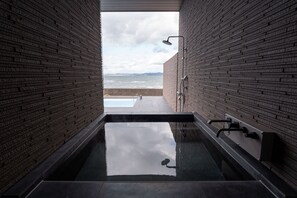Une salle de bain moderne avec un jacuzzi entouré de parois en verre, des murs en briques et une vue sur la mer.