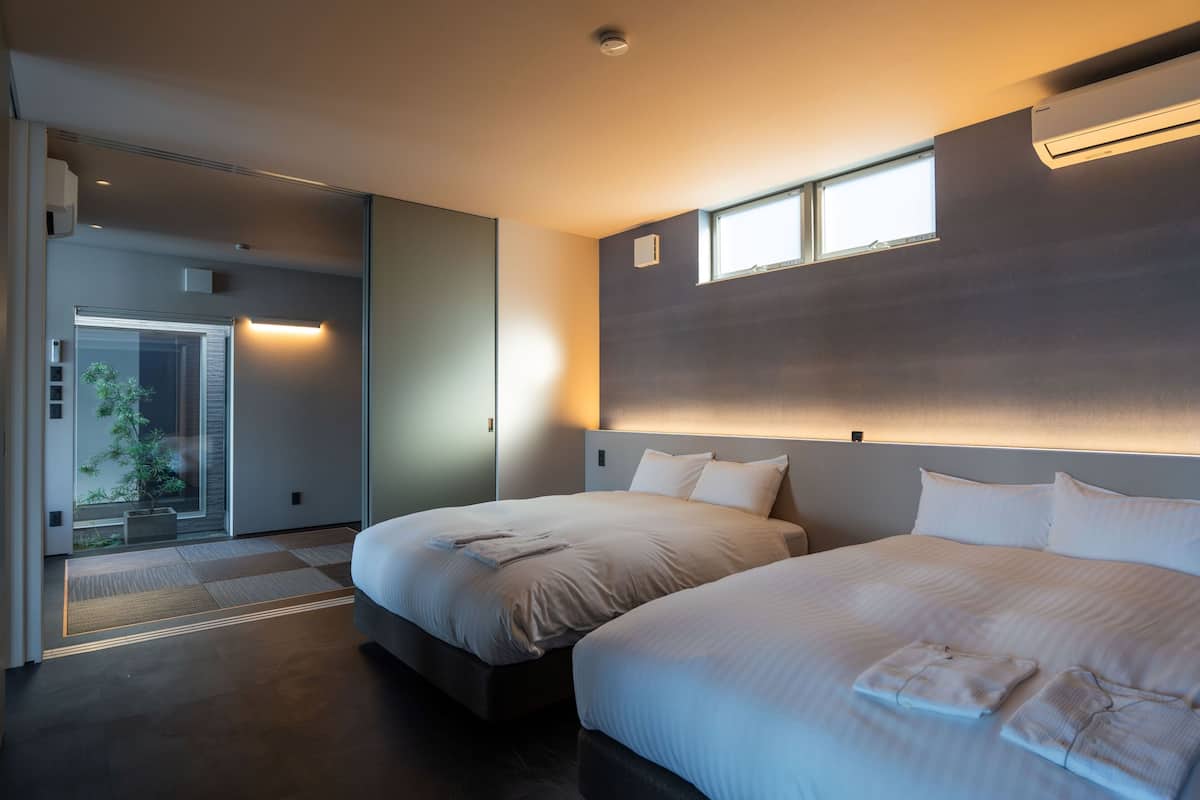 Une chambre d’hôtel moderne avec deux lits, une grande fenêtre et une porte coulissante donnant sur un balcon.