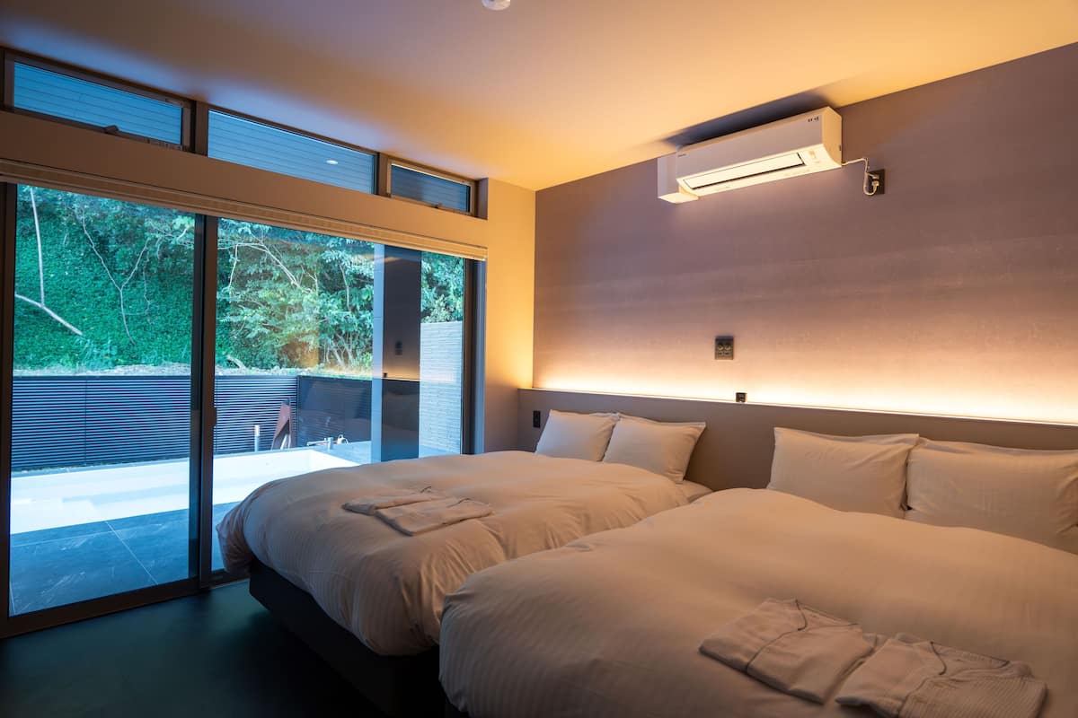 Une chambre d’hôtel moderne dotée d’un grand lit, d’une porte-fenêtre coulissante donnant sur un espace extérieur et d’un système de climatisation intégré.