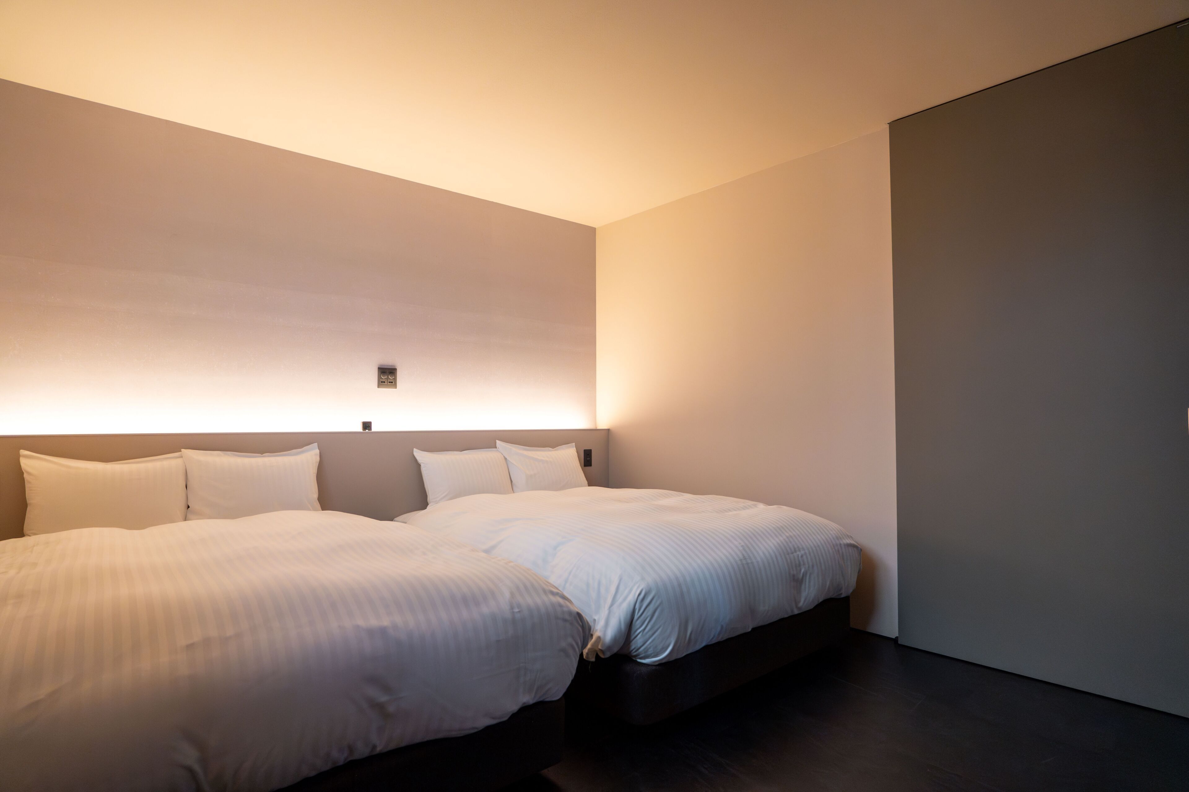 Ein modernes Hotelzimmer mit zwei Betten, dunklem Boden und einer Wandleuchte.