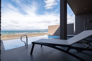 Un espace aménagé au bord de la piscine, offrant une vue sur l’océan, avec un fauteuil de relaxation et une architecture moderne.