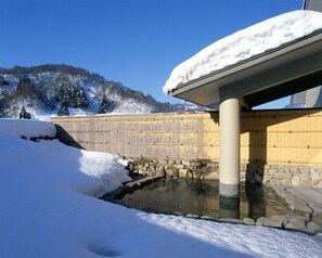 A snow-covered outdoor area with a stone wall, a wooden fence, and a small water feature. - Kuwadori Yuttari Village (Joetsu)