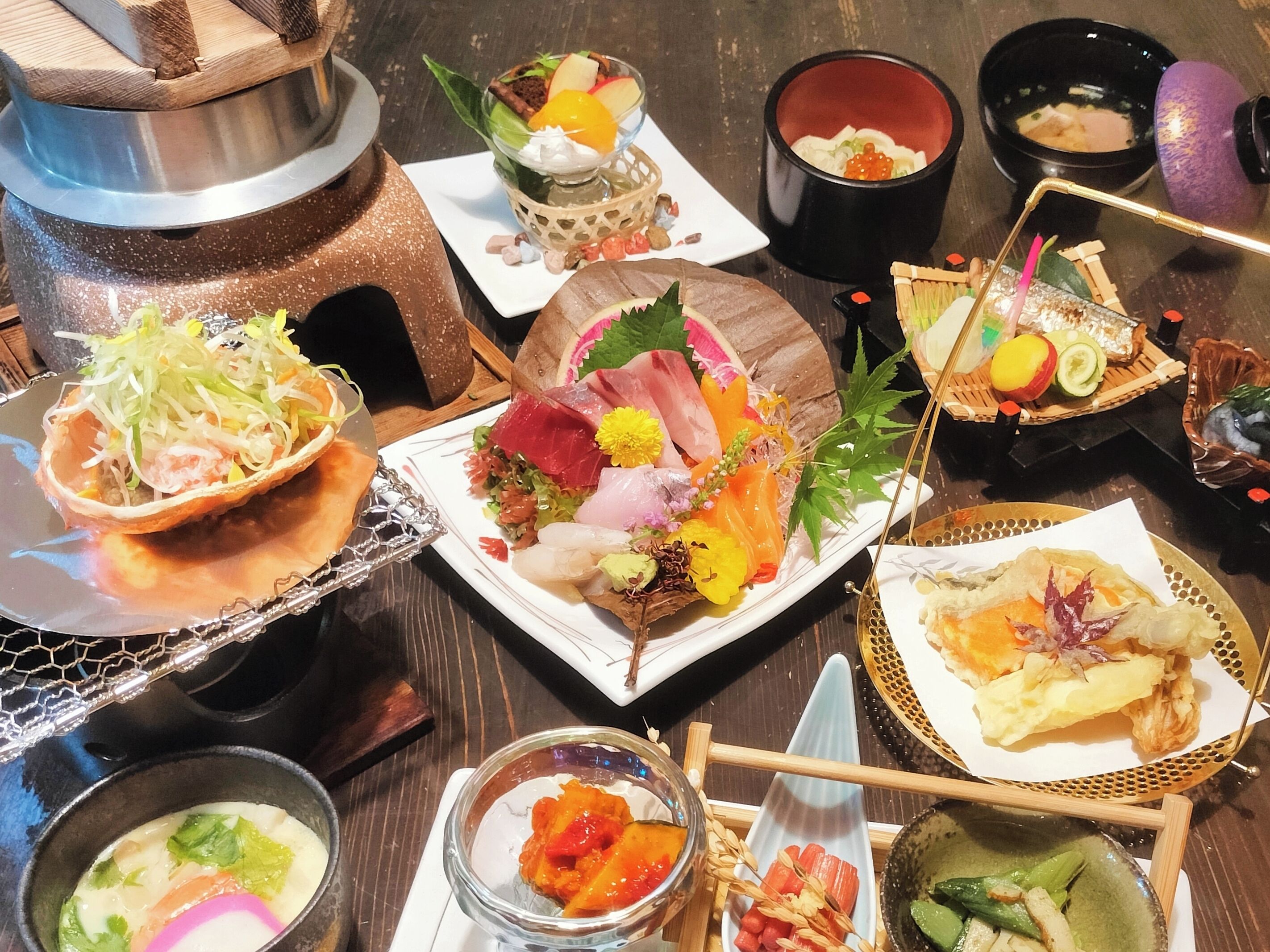 Verschiedene Gerichte auf einem Holztisch, darunter Sushi, Tempura und ein Fondue.