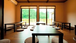 A room with a long table and benches, large windows, and a view of greenery outside.