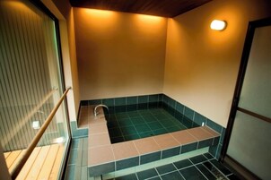 Un baño pequeño y cerrado con bañera, ducha y ventana con persianas.