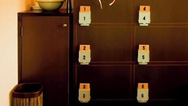 A bathroom with a sink, a trash bin, a cabinet with numbered blocks, and a vase with pink flowers.