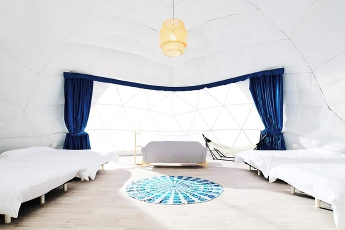 A modern, dome-shaped room with two beds, a central seating area, and a large window with curtains.