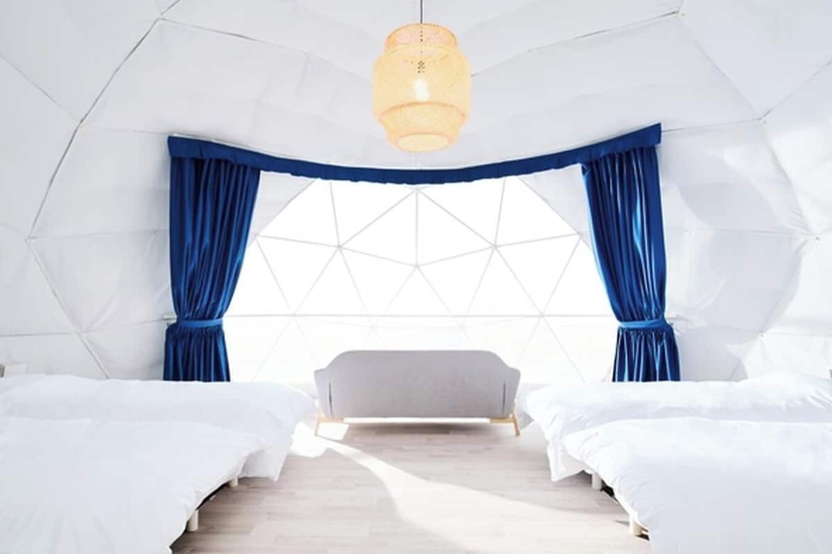 A modern, geometric-themed bedroom with two beds, a large window, and a hanging light fixture.