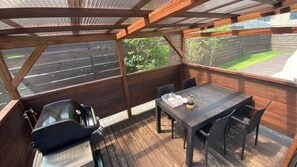 An outdoor deck with a table and chairs, a grill, and a view of the backyard.