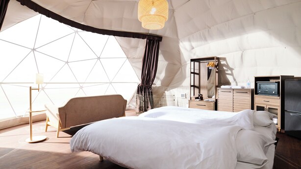 A tented room with a bed, a hanging light fixture, a desk with a computer, and a window with a geometric view. - Eight Village (Kujukuri)