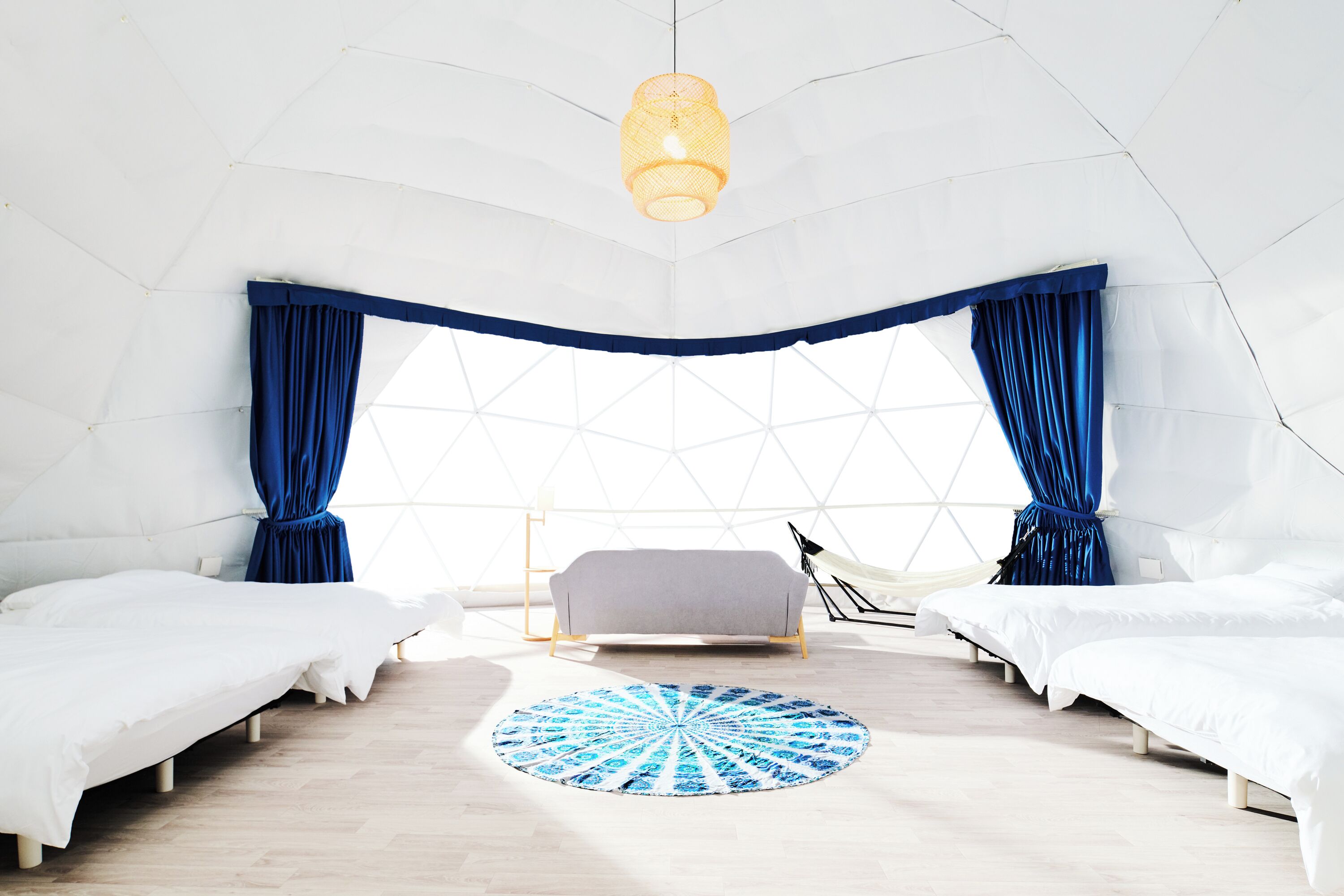 A tented room with two beds, a central sofa, a patterned rug, and a hanging light fixture.