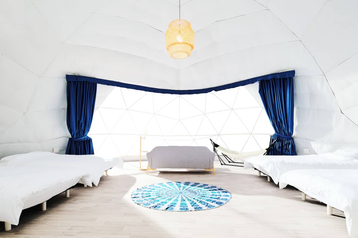 A tented room with two beds, a central sofa, a patterned rug, and a hanging light fixture.