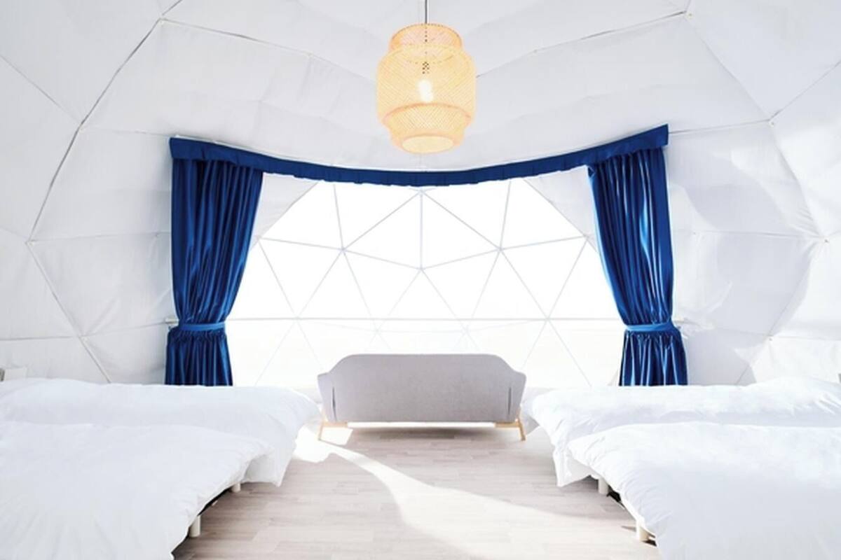 A modern, geometric-themed bedroom with two beds, a large window, and a hanging light fixture.