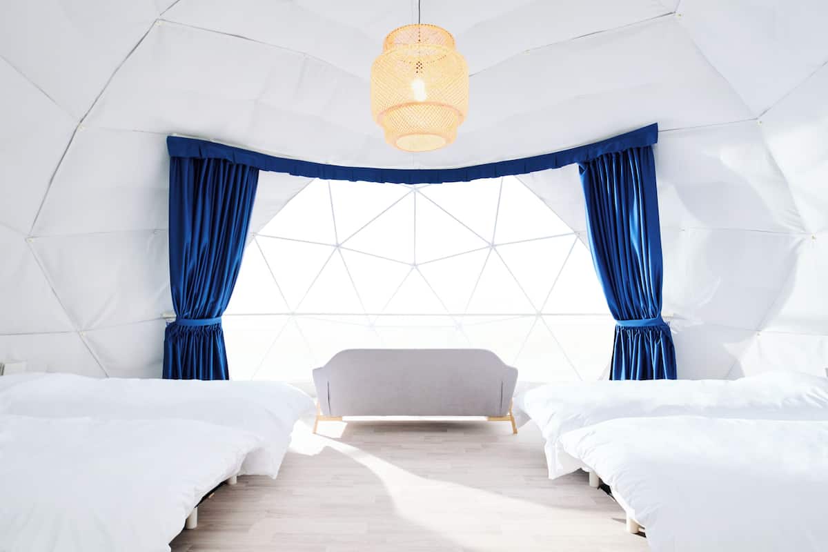A modern, geometric-themed room with a large window, two beds, and a hanging light fixture.