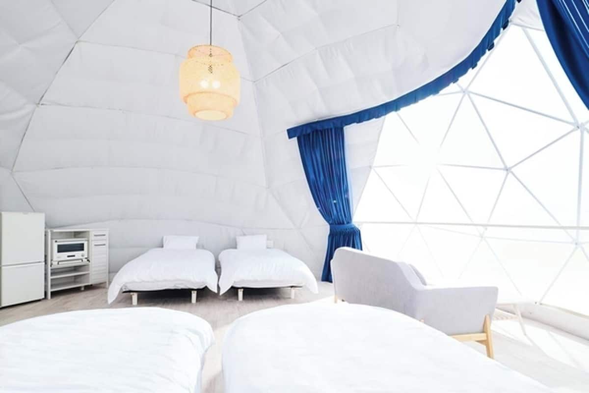 A modern, spacious tent-style room with two beds, a desk, and a chair.