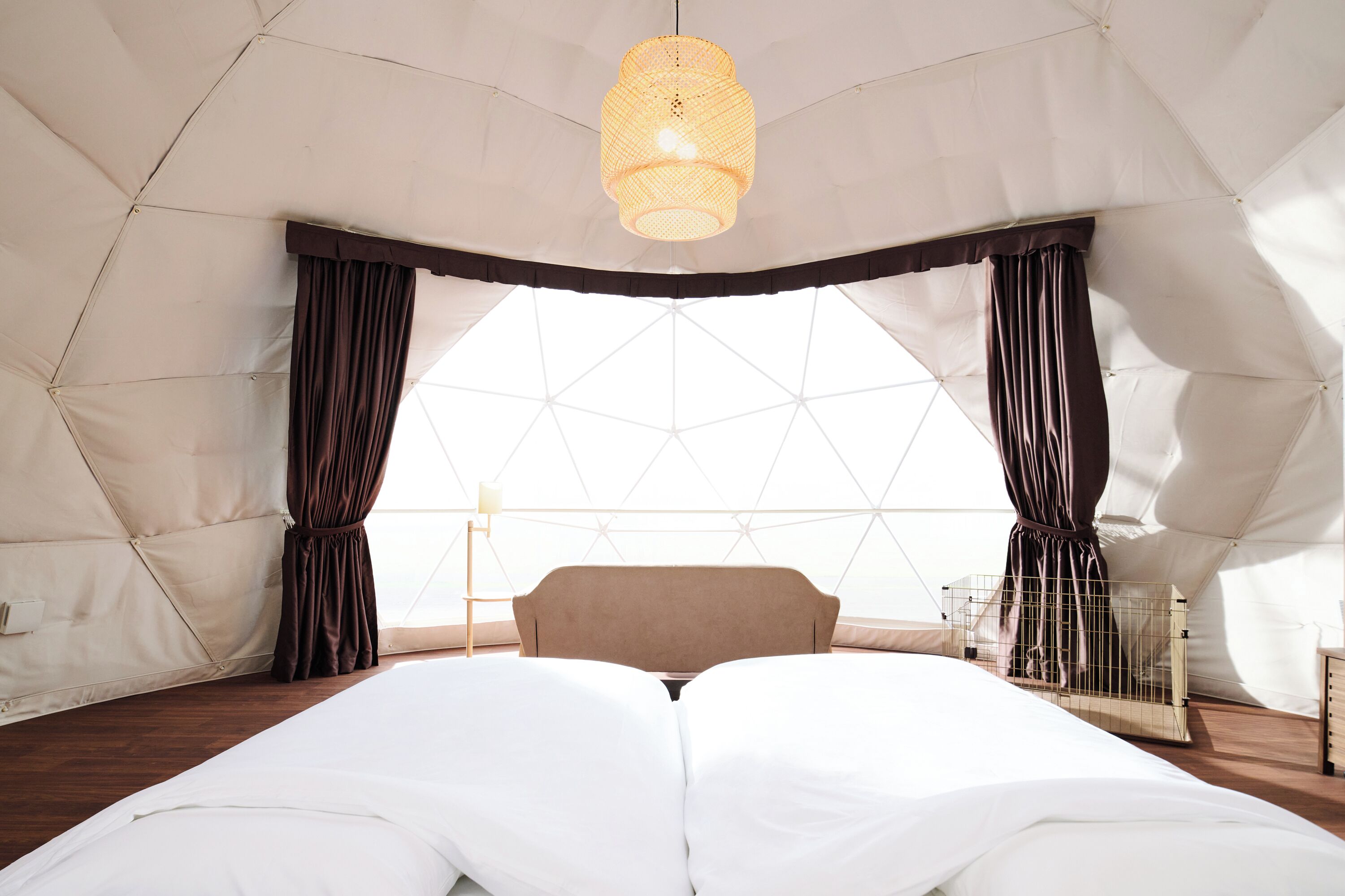 A tented room with a bed, curtains, a hanging light fixture, and a view through a geometric window.