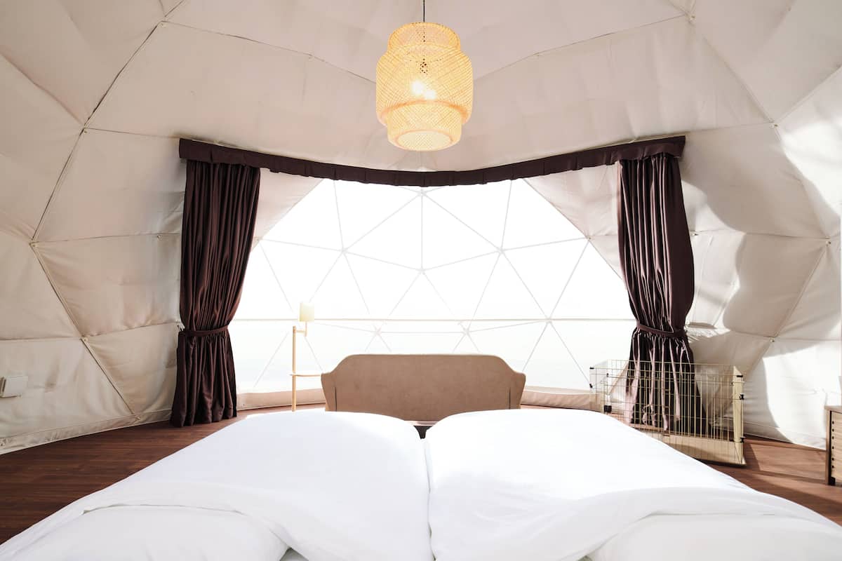A tented room with a bed, curtains, a hanging light fixture, and a view through a geometric window.