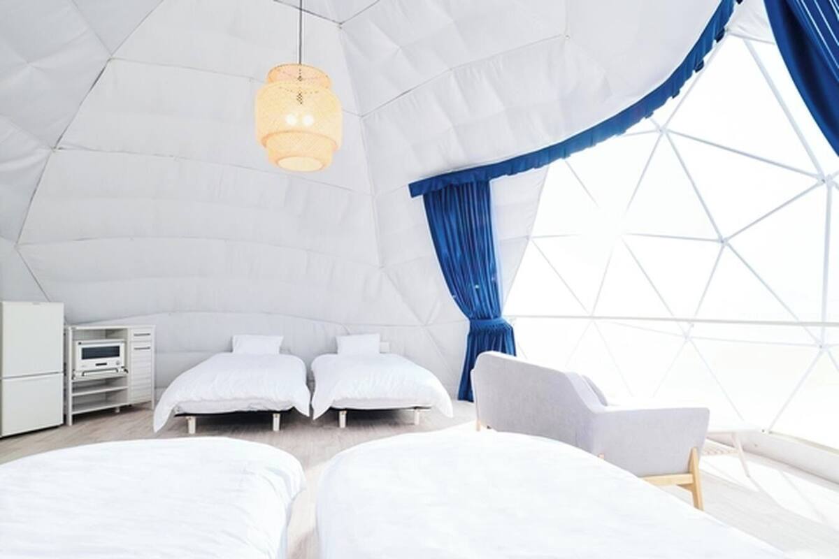 A modern, spacious tent-style room with two beds, a desk, and a chair.