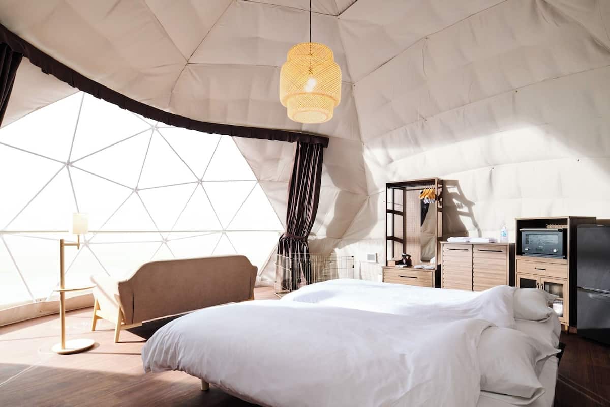 A spacious tented room with a bed, a chair, a desk with a computer, and a television.