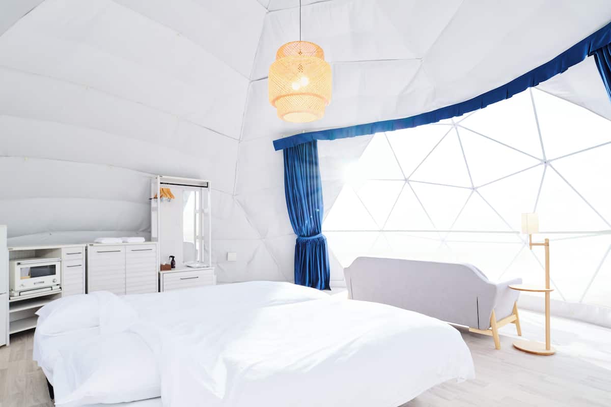 A modern, well-lit bedroom with a bed, bedside table, and a large window.
