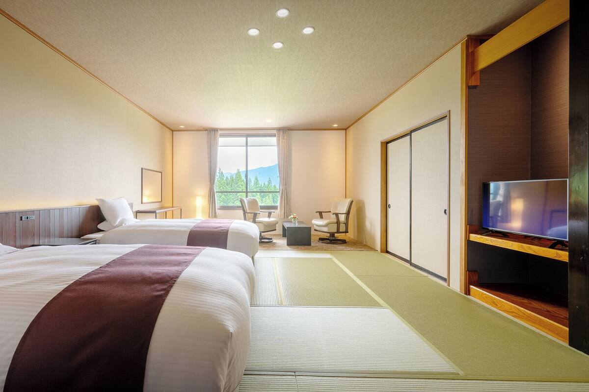 A hotel room with two beds, a TV, a desk, and a view of the outdoors.