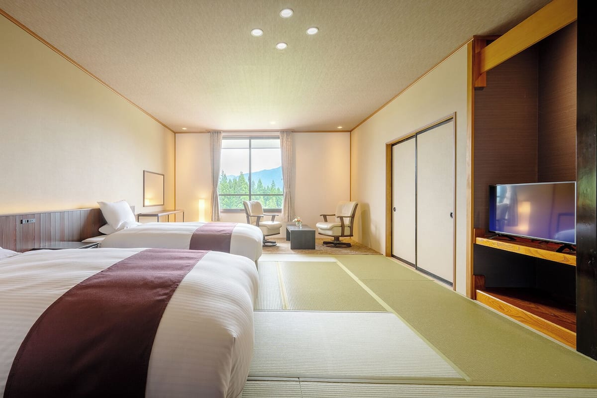 A hotel room with two beds, a TV, a desk, and a view of the outdoors.