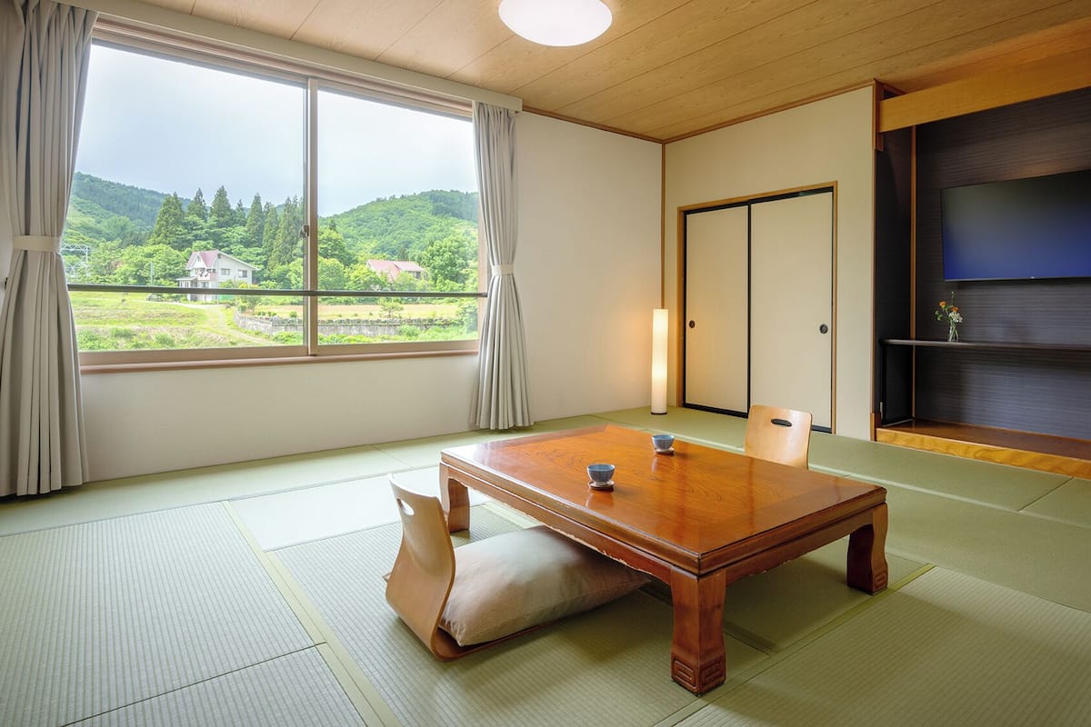 A traditional Japanese room with tatami flooring, a wooden table with two bowls, a sliding door, and a TV on a dark wall.