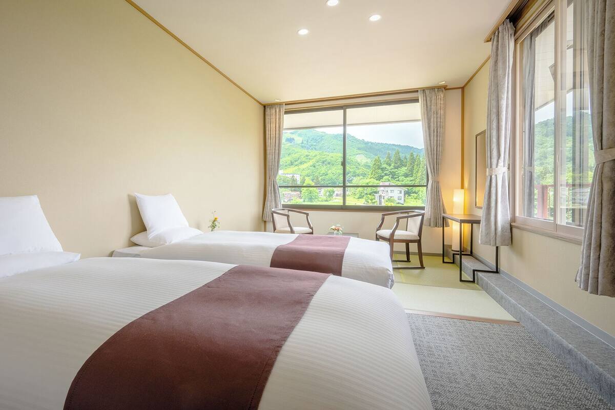 A hotel room with two beds, a desk, and a view of greenery.